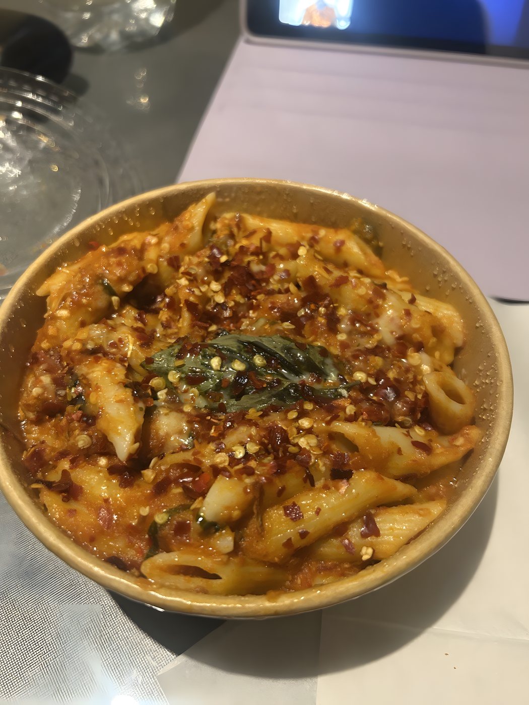 A bowl of penne pasta in a rich tomato sauce topped with chilli flakes and fresh basil